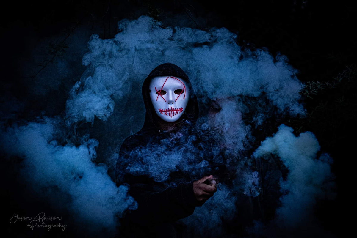 Man wearing scary Halloween mask holding blue smoke bomb  